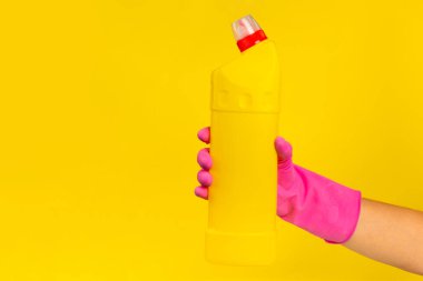 Sarı arka planda temizlik ürünleri tutan lastik eldivenli bir el. Pankart. Temizlik kavramı.