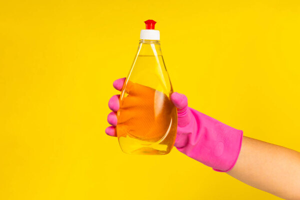 Hand with  rubber glove holding cleaning products on a yellow background. banner. Cleaning concept.