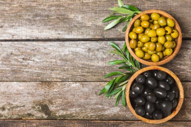 Beyaz ahşap arka planda yeşil ve siyah zeytinler. Taze zeytin yapraklı zeytin yağı ve kâse içinde çeşitli zeytin türleri. Uzayı kopyala Mesaj için yer. Akdeniz yemekleri. Vejetaryen.
