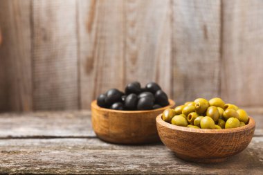 Beyaz ahşap arka planda yeşil ve siyah zeytinler. Taze zeytin yapraklı zeytin yağı ve kâse içinde çeşitli zeytin türleri. Uzayı kopyala Mesaj için yer. Akdeniz yemekleri. Vejetaryen.