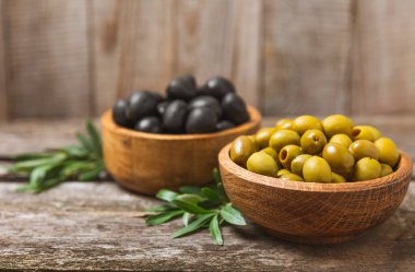 Beyaz ahşap arka planda yeşil ve siyah zeytinler. Taze zeytin yapraklı zeytin yağı ve kâse içinde çeşitli zeytin türleri. Uzayı kopyala Mesaj için yer. Akdeniz yemekleri. Vejetaryen.