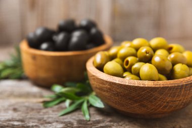Beyaz ahşap arka planda yeşil ve siyah zeytinler. Taze zeytin yapraklı zeytin yağı ve kâse içinde çeşitli zeytin türleri. Uzayı kopyala Mesaj için yer. Akdeniz yemekleri. Vejetaryen.