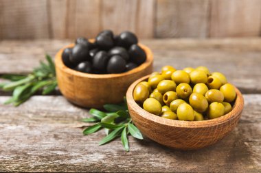 Beyaz ahşap arka planda yeşil ve siyah zeytinler. Taze zeytin yapraklı zeytin yağı ve kâse içinde çeşitli zeytin türleri. Uzayı kopyala Mesaj için yer. Akdeniz yemekleri. Vejetaryen.