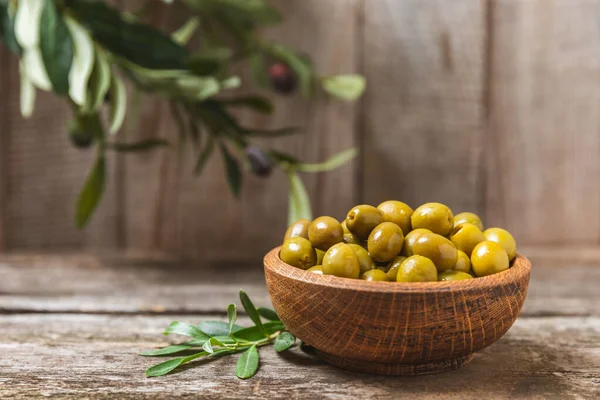 Green olives on a white wooden background. Various types of olives in bowls and olive oil with fresh olive leaves. Copy space. Place for text. Mediterranean food. Vegan.