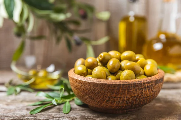 Green olives on a white wooden background. Various types of olives in bowls and olive oil with fresh olive leaves. Copy space. Place for text. Mediterranean food. Vegan.