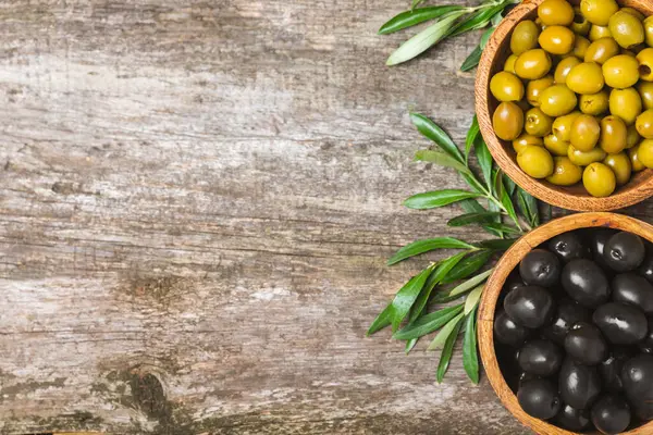 Green and black olives on a white wooden background. Various types of olives in bowls and olive oil with fresh olive leaves. Copy space. Place for text. Mediterranean food. Vegan.
