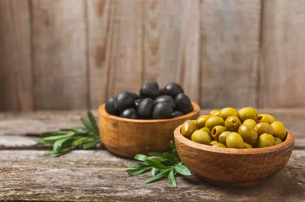 Green and black olives on a white wooden background. Various types of olives in bowls and olive oil with fresh olive leaves. Copy space. Place for text. Mediterranean food. Vegan.