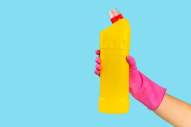Plastik koruyucu eldivenli bir temizlikçinin elinde mavi arka planda bir şişe temizlik kimyasalı bulunur. Ticari temizlik şirketi. Bahar temizliği. Metin veya logo için boşluk.