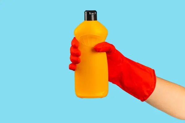 A cleaner\'s hand in a rubber protective glove holds a bottle of cleaning chemical on a blue background. Commercial cleaning company. Spring regular cleaning. Space for text or logo.