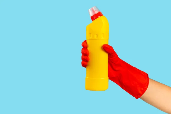A cleaner's hand in a rubber protective glove holds a bottle of cleaning chemical on a blue background. Commercial cleaning company. Spring regular cleaning. Space for text or logo.