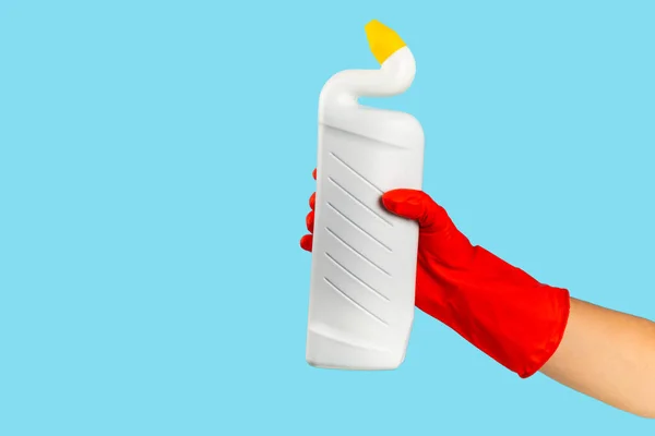 A cleaner\'s hand in a rubber protective glove holds a bottle of cleaning chemical on a blue background. Commercial cleaning company. Spring regular cleaning. Space for text or logo.