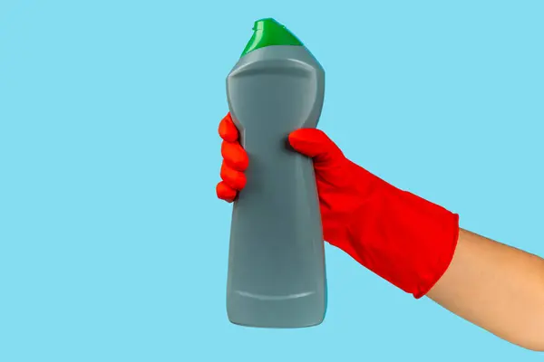 A cleaner's hand in a rubber protective glove holds a bottle of cleaning chemical on a blue background. Commercial cleaning company. Spring regular cleaning. Space for text or logo.