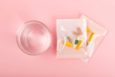 Vitaminler ve takviyeler. Arka planda bir bardak su bulunan çeşitli vitamin hapları. Her gün için multivitamin kompleksi. Besleyici takviyeler. İlaçlarını almanın zamanı geldi. Düz yatıyordu. Metin için boşluk. Boşluğu kopyala