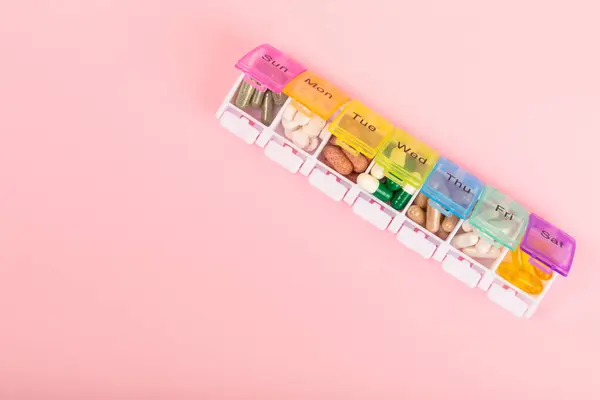 Vitamins and supplements. Variety of vitamin tablets in a pillbox on a pink background. Multivitamins for every day. Nutritional supplements. Flat lay. Space for text.Copy space
