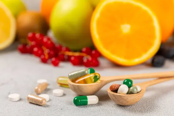 Vitamins and supplements. Variety of vitamin tablets in a wooden spoon on a texture background.Multivitamins with fresh and healthy fruits.Food supplements. Flat lay. Space for text.Copy space