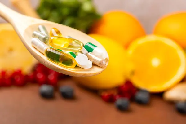 Vitamins and supplements. Variety of vitamin tablets in a wooden spoon on a texture background.Multivitamins with fresh and healthy fruits.Food supplements. Flat lay. Space for text.Copy space