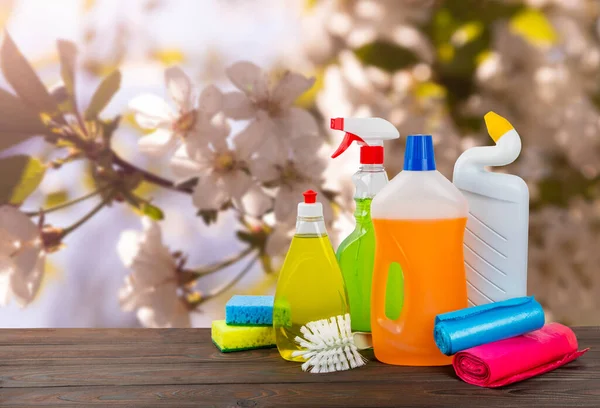 Spring cleaning concept.Cleaning products on blurred nature background.Cleaning products on wooden table.Household chemicals.Cleaning and detergents in plastic bottles, sponges and gloves.Mockup.