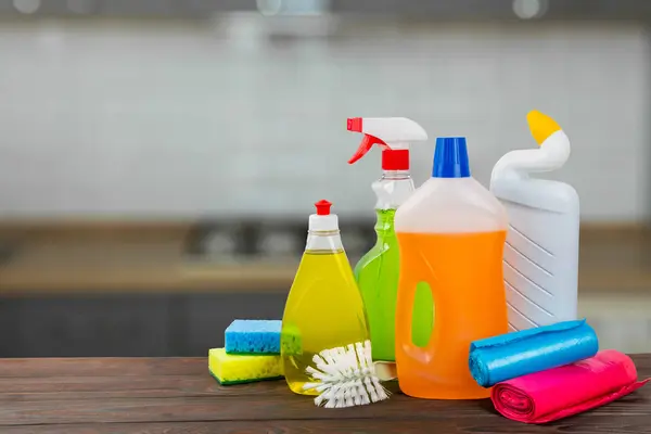 Cleaning products on a wooden table on a blurred kitchen background. Cleaning service concept. Household chemicals.Cleaning and detergents in plastic bottles, sponges and gloves.Mockup. Design. copy space.place for text.