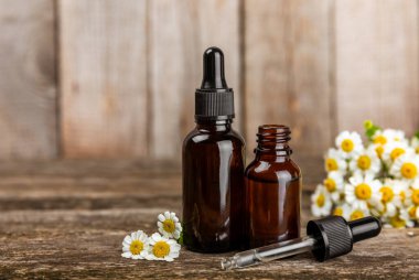 Eski ahşap arka planda papatya yağı bulunan cam şişe. Papatya çiçekleri, yaklaşın. Aromaterapi, spa ve bitkisel ilaç malzemeleri. Güzellik konsepti. Uzayı kopyala. Doğal Kozmetik