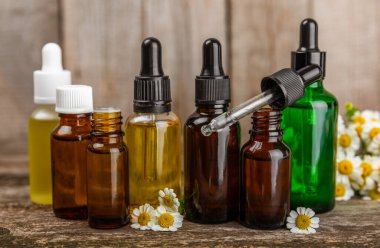 Eski ahşap arka planda papatya yağı bulunan cam şişe. Papatya çiçekleri, yaklaşın. Aromaterapi, spa ve bitkisel ilaç malzemeleri. Güzellik konsepti. Uzayı kopyala. Doğal Kozmetik