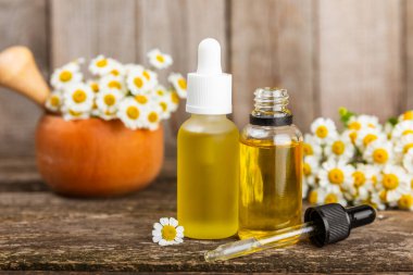 Eski ahşap arka planda papatya yağı bulunan cam şişe. Papatya çiçekleri, yaklaşın. Aromaterapi, spa ve bitkisel ilaç malzemeleri. Güzellik konsepti. Uzayı kopyala. Doğal Kozmetik