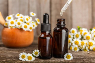 Eski ahşap arka planda papatya yağı bulunan cam şişe. Papatya çiçekleri, yaklaşın. Aromaterapi, spa ve bitkisel ilaç malzemeleri. Güzellik konsepti. Uzayı kopyala. Doğal Kozmetik