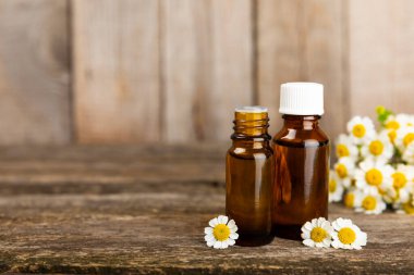 Eski ahşap arka planda papatya yağı bulunan cam şişe. Papatya çiçekleri, yaklaşın. Aromaterapi, spa ve bitkisel ilaç malzemeleri. Güzellik konsepti. Uzayı kopyala. Doğal Kozmetik