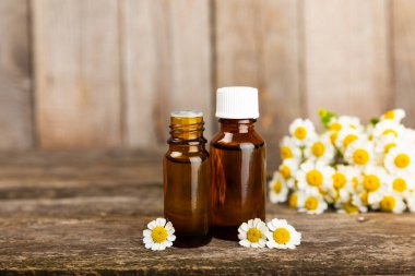 Eski ahşap arka planda papatya yağı bulunan cam şişe. Papatya çiçekleri, yaklaşın. Aromaterapi, spa ve bitkisel ilaç malzemeleri. Güzellik konsepti. Uzayı kopyala. Doğal Kozmetik
