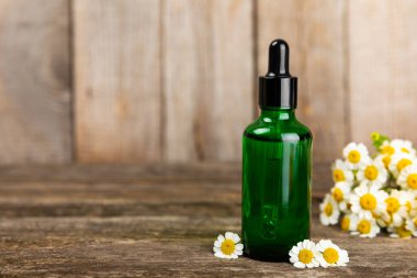 Eski ahşap arka planda papatya yağı bulunan cam şişe. Papatya çiçekleri, yaklaşın. Aromaterapi, spa ve bitkisel ilaç malzemeleri. Güzellik konsepti. Uzayı kopyala. Doğal Kozmetik