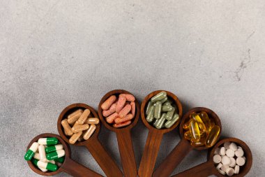 Vitaminler ve takviyeler. Ahşap kaşıklardaki vitamin tabletlerinin dokulu arka planda çeşitliliği. Her gün için multivitamin kompleksi. Besleyici takviyeler. Boşluğu kopyala. Bağışıklık için vitaminler.