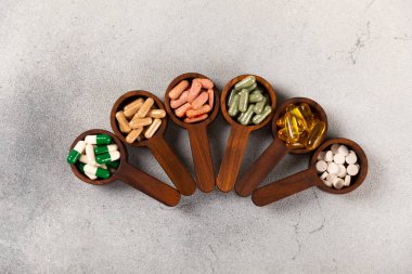Vitaminler ve takviyeler. Ahşap kaşıklardaki vitamin tabletlerinin dokulu arka planda çeşitliliği. Her gün için multivitamin kompleksi. Besleyici takviyeler. Boşluğu kopyala. Bağışıklık için vitaminler.