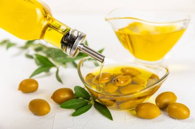 Beyaz dokuya sahip bir şişede zeytin yağı. Zeytin dallı ve meyveli yağ şişesi. Mesaj için yer. kopyalama alanı. Yemek yağı ve salata sosu..