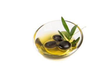 Bir kase taze zeytinyağı ve beyaz arka planda yapraklı zeytin. Cam kasede nefis zeytinyağı. Zeytin yağı şişesi.