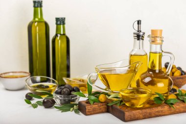 Beyaz dokuya sahip bir şişede zeytin yağı. Zeytin dallı ve meyveli yağ şişesi. Mesaj için yer. kopyalama alanı. Yemek yağı ve salata sosu..