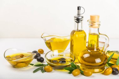 Beyaz dokuya sahip bir şişede zeytin yağı. Zeytin dallı ve meyveli yağ şişesi. Mesaj için yer. kopyalama alanı. Yemek yağı ve salata sosu..
