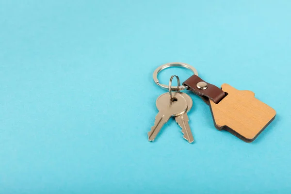 Keychain in the shape of a house with a key ring on a blue background. Concepts for real estate and moving home or renting property. Buying a property. Mock-up keychain house shaped.Copy space.