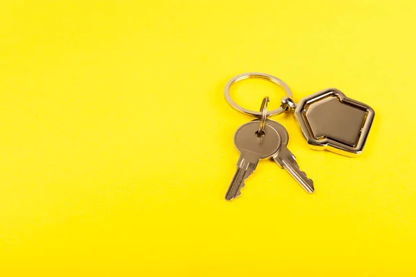 Keychain in the shape of a house with a key ring on a yellow background. Concepts for real estate and moving home or renting property. Buying a property. Mock-up keychain house shaped.Copy space.