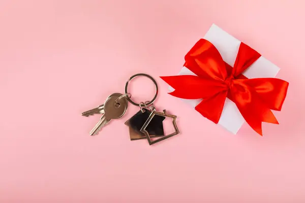 Keychain in the shape of a house with a key ring on a pink background. Concepts for real estate and moving home or renting property. Buying a property. Mock-up keychain house shaped.Copy space.
