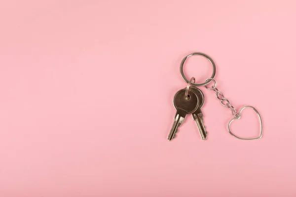 Keychain in the shape of a heart with a key ring on a pink background. Concepts for real estate and moving home or renting property. Buying a property. Mock-up keychain.Copy space.