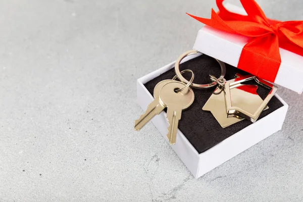 Keychain in the shape of a house with a key ring on a gray background. Concepts for real estate and moving home or renting property. Buying a property. Mock-up keychain house shaped.Copy space.