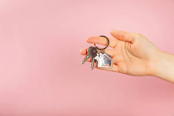 Keychain in the shape of a house with a key ring on a pink background. Concepts for real estate and moving home or renting property. Buying a property. Mock-up keychain house shaped.Copy space.