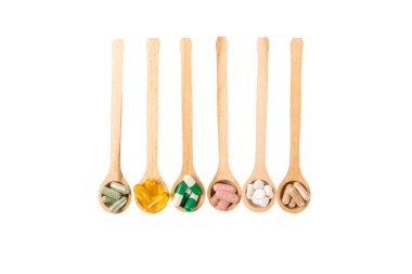 Vitaminler ve takviyeler. Beyaz arka planda izole edilmiş tahta kaşıklardaki çeşitli vitamin hapları. Her gün için multivitamin kompleksi. Besleyici takviyeler. Boşluğu kopyala. Bağışıklık için vitaminler.