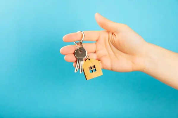 Keychain with a key ring in hand on a blue background. Concepts for real estate and moving home or renting property. Buying a property. Mock-up keychain.Copy space.