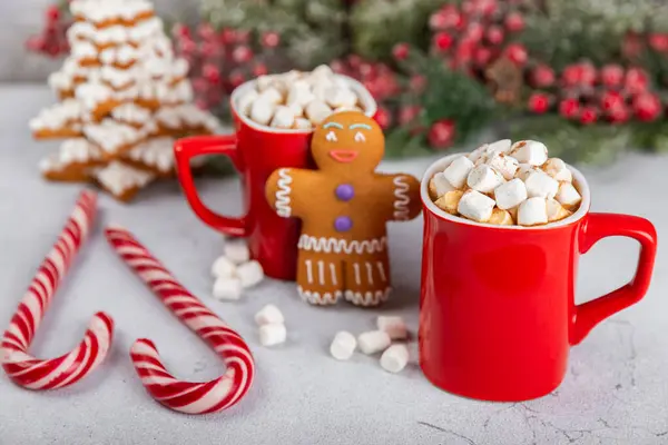 Hot drink with marshmallows and candy cane in a red cup on a texture table.Cozy seasonal holidays.Hot cocoa with gingerbread Christmas cookies.Hot chocolate with marshmallow and spices.Copy space.