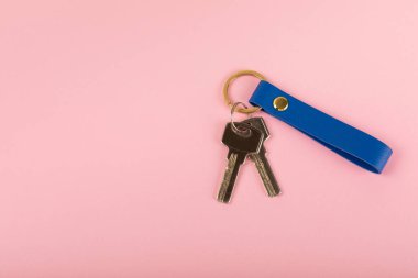 Pembe arka planda anahtarlığı olan deri bir anahtarlık. Gayrimenkul ve eve taşınma ya da mülk kiralama kavramları. Mülk almak. Model anahtarlık. Boşluğu kopyala.