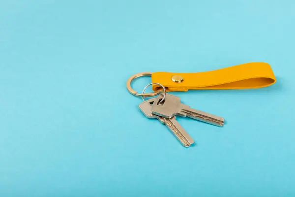 Leather keychain with a key ring on a blue background. Concepts for real estate and moving home or renting property. Buying a property. Mock-up keychain.Copy space.