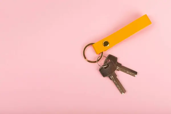 Leather keychain with a key ring on a pink background. Concepts for real estate and moving home or renting property. Buying a property. Mock-up keychain.Copy space.