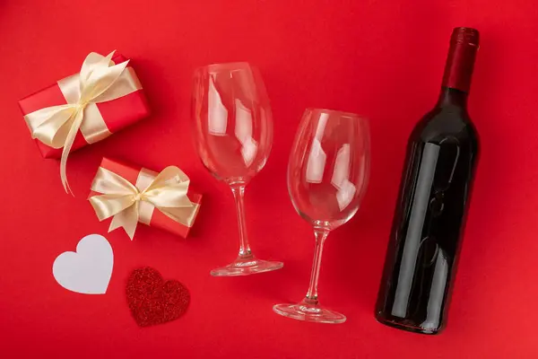 Valentine\'s Day concept. Valentine\'s Day background. Gifts, candles, confetti, envelope - postcard, candy, glasses, wine and a bouquet of roses on a red background. Flatley.Valentine\'s day celebration