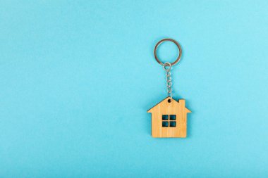 Anahtar zinciri, arka planında anahtarlık olan bir ev şeklinde. Gayrimenkul ve eve taşınma ya da mülk kiralama kavramları. Mülk almak. Model anahtarlık şeklinde ev.