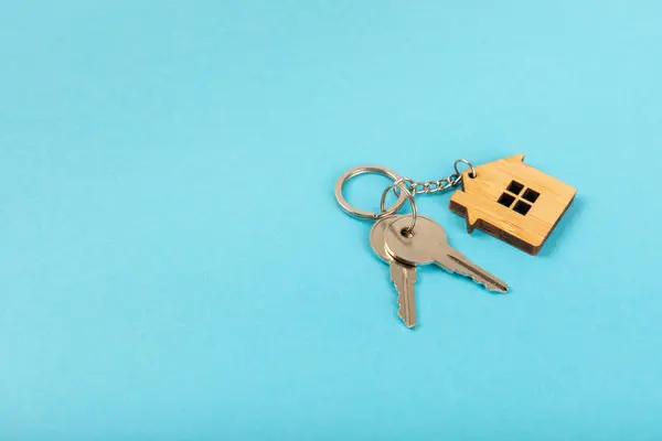 Keychain in the shape of a house with a key ring on a textured background. Concepts for real estate and moving home or renting property. Buying a property. Mock-up keychain house shaped.